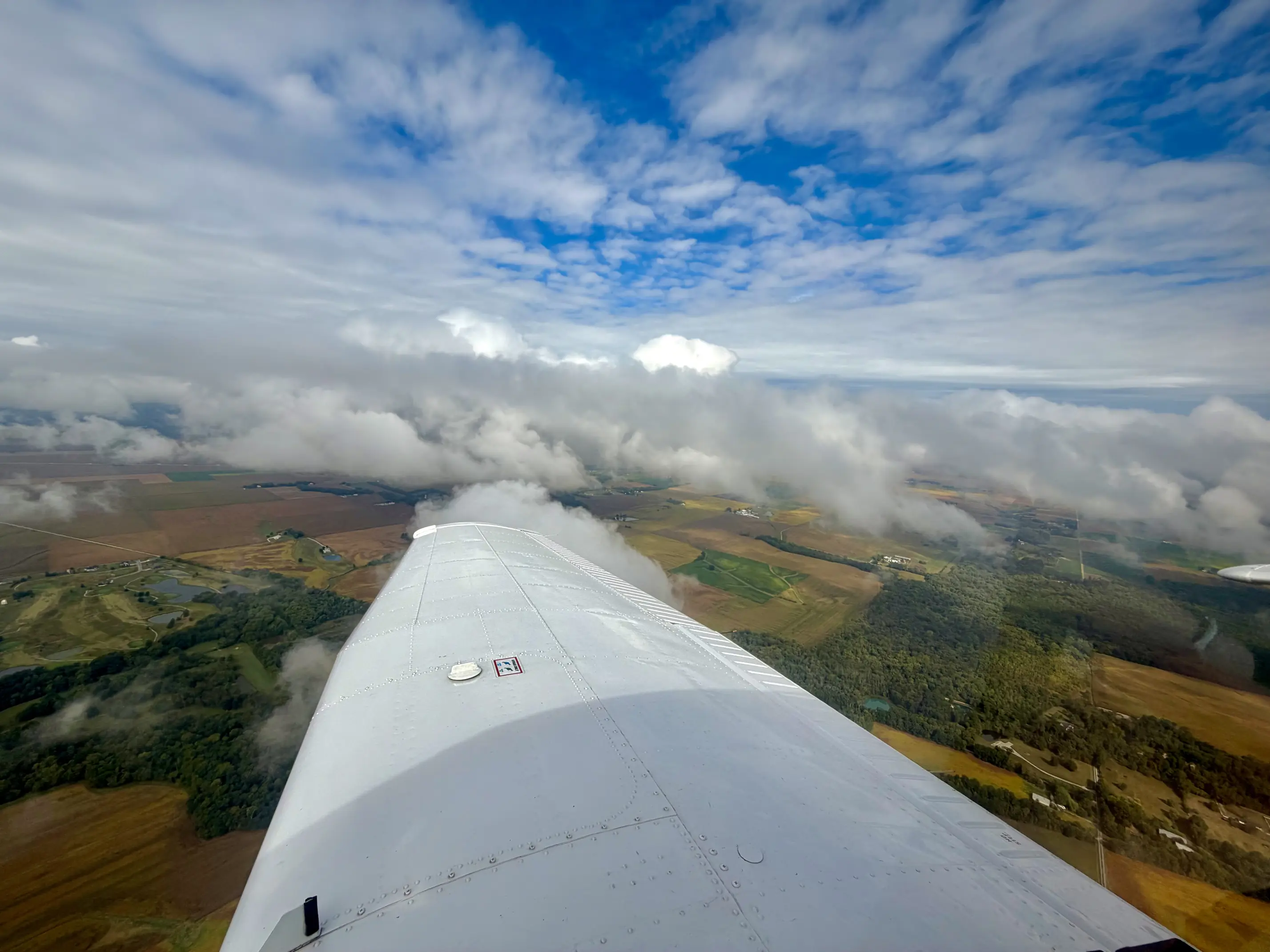 View over the wing of an Ideal Aviation airplane with building clouds over Illinois farmland