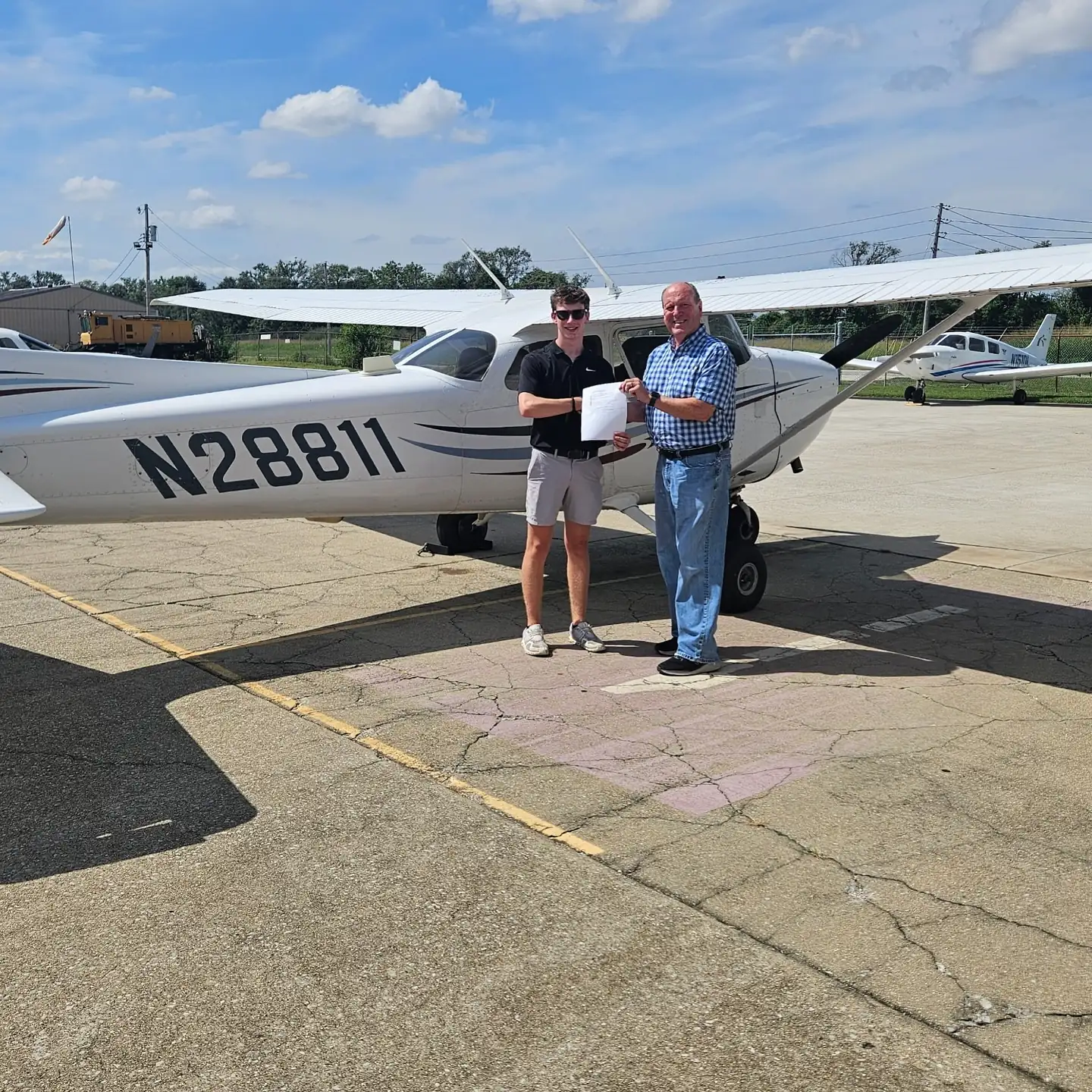 Designated Pilot Examiner handing a temporary certificate to an Ideal Aviation student beside a Cessna 172 after a checkride