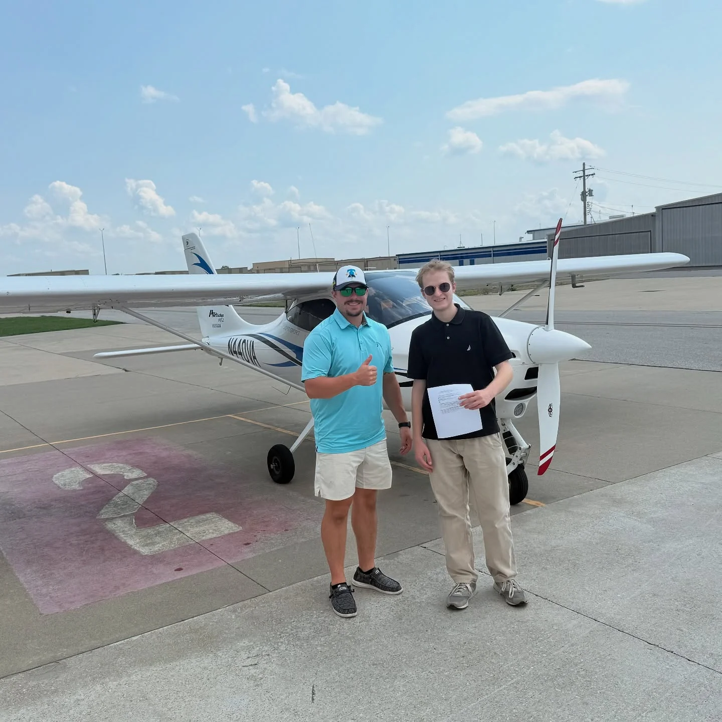 Ideal Aviation instructor giving a thumbs up beside a student holding checkride paperwork in front of a Tecnam P92