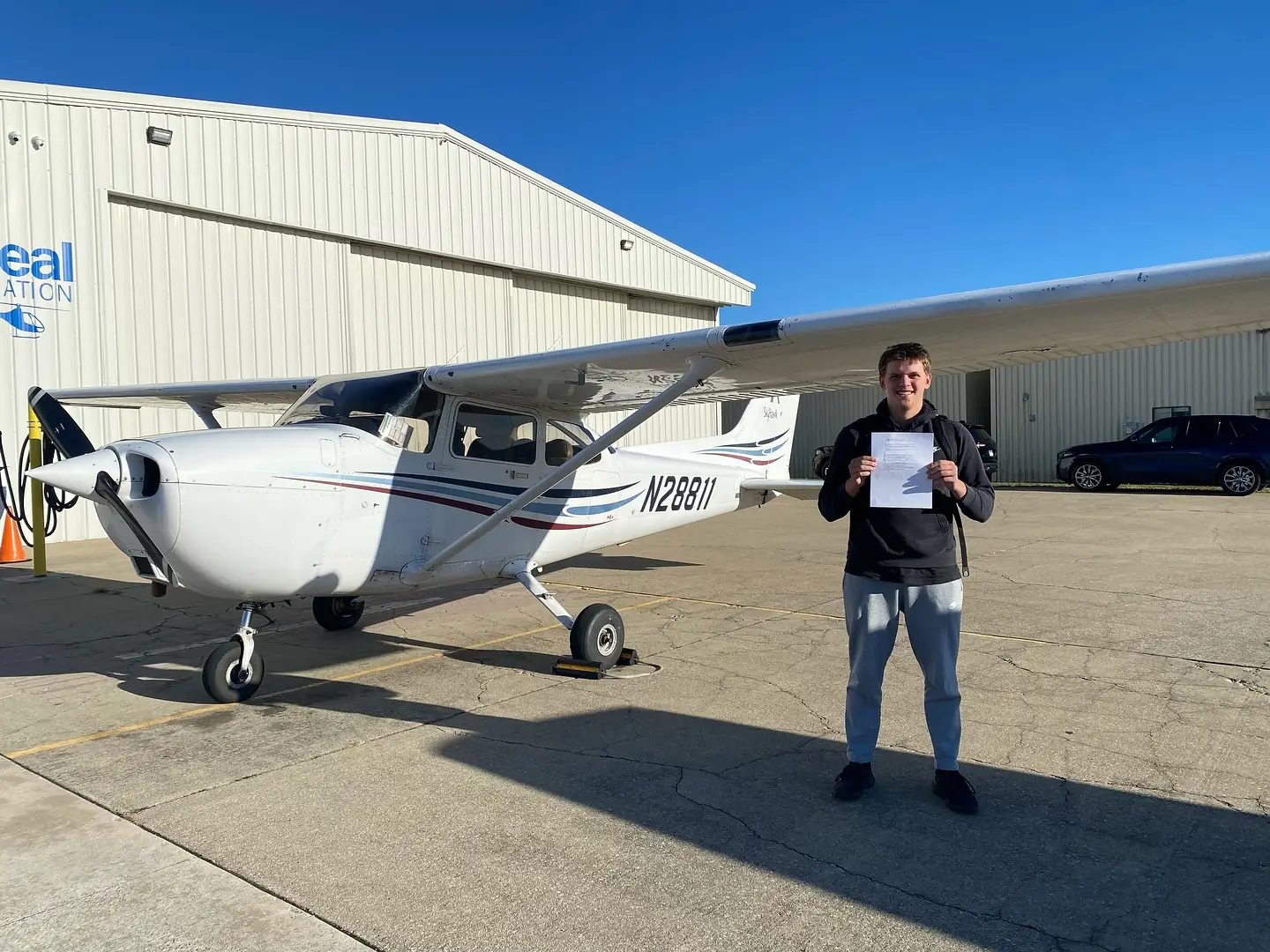Ideal Aviation student holding a new pilot certificate beside a Cessna inside the hangar